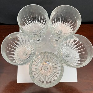 May include: Set of five clear glass wine glasses with a cut glass design. The glasses are arranged in a circle with the stems pointing outwards.