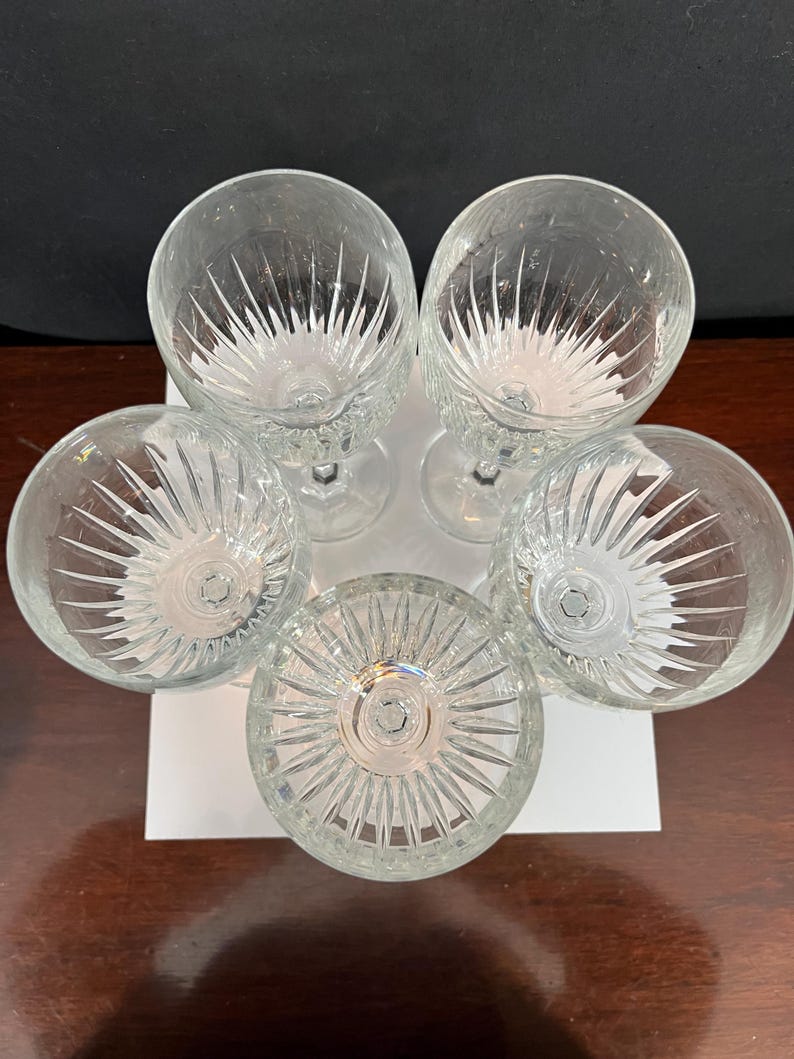 May include: Set of five clear glass wine glasses with a cut glass design. The glasses are arranged in a circle with the stems pointing outwards.