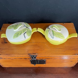 May include: Two vintage ceramic serving dishes with lids. The dishes are a bright yellow color with a green and white floral design. The dishes are sitting on a wooden box.