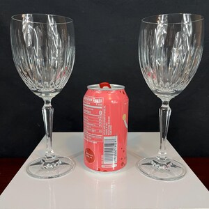 May include: Two clear glass wine glasses with a fluted design. The glasses are on a white surface with a pink can in the centre.