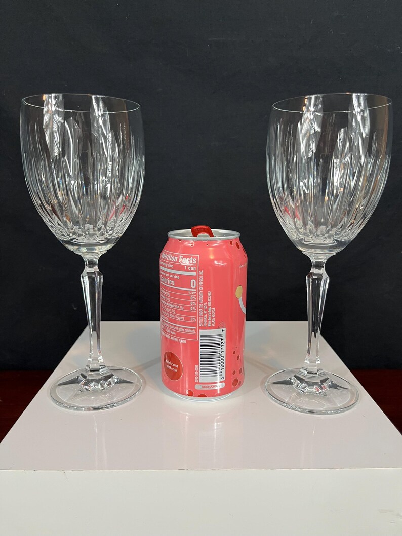 May include: Two clear glass wine glasses with a fluted design. The glasses are on a white surface with a pink can in the centre.