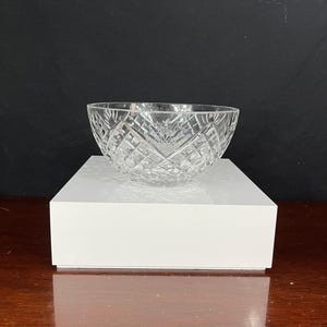 Puede incluir: Un cuenco de vidrio transparente con un patr&oacute;n de diamante se encuentra sobre un pedestal blanco. El cuenco est&aacute; vac&iacute;o y tiene una superficie reflectante.