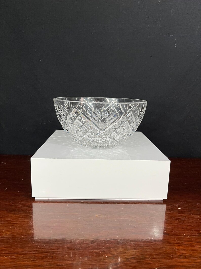 Puede incluir: Un cuenco de vidrio transparente con un patr&oacute;n de diamante se encuentra sobre un pedestal blanco. El cuenco est&aacute; vac&iacute;o y tiene una superficie reflectante.