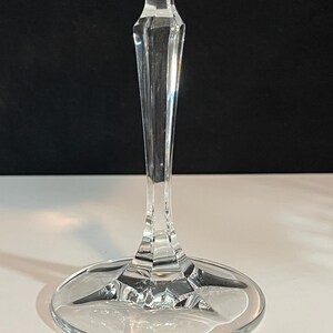 May include: A clear glass wine glass with a tall, slender stem and a wide, round base. The glass has a simple, elegant design.