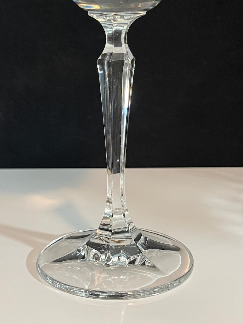 May include: A clear glass wine glass with a tall, slender stem and a wide, round base. The glass has a simple, elegant design.