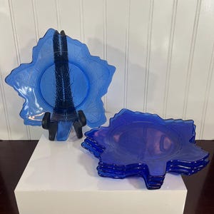 May include: Four cobalt blue glass plates with a leaf design. The plates are stacked on top of each other.