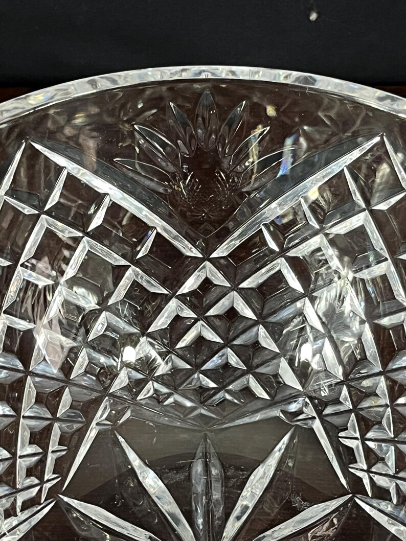 Puede incluir: Un cuenco de vidrio transparente con un dise&ntilde;o de cristal tallado. El cuenco tiene una forma ancha y poco profunda y un patr&oacute;n decorativo de formas geom&eacute;tricas.