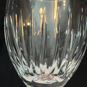 May include: A clear glass wine glass with a cut crystal design. The glass has a round bowl and a long stem.