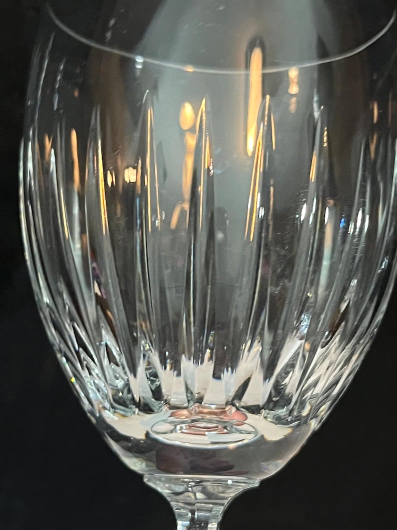 May include: A clear glass wine glass with a cut crystal design. The glass has a round bowl and a long stem.