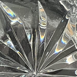 Puede incluir: Primer plano de un cuenco de vidrio transparente con un dise&ntilde;o de vidrio cortado. El cuenco tiene un patr&oacute;n de estrella con un punto central en el medio. El vidrio refleja la luz, creando un efecto arco&iacute;ris.