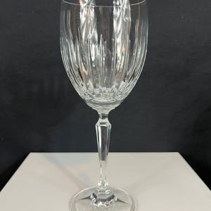 May include: A clear glass wine glass with a tall, slender stem and a wide bowl. The bowl has a decorative, vertical, cut-glass pattern.