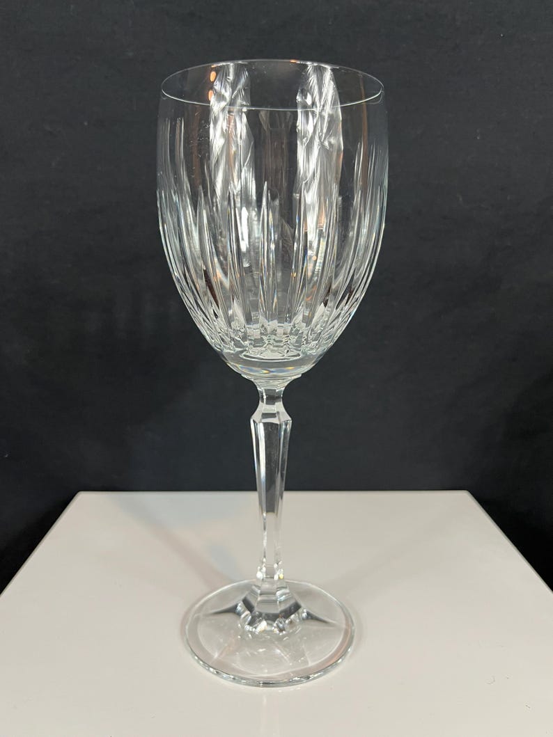 May include: A clear glass wine glass with a tall, slender stem and a wide bowl. The bowl has a decorative, vertical, cut-glass pattern.