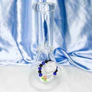 May include: Clear glass water pipe with a wide base and a narrow neck. A decorative band of black and blue beads encircles the bowl. The word "HIGH" is spelled out with colorful letter beads on the side of the pipe.