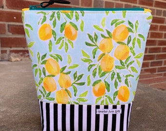 May include: A light blue zippered pouch with a lemon print and black and white stripes. The pouch has a black zipper pull and a label that reads "Quarter Acre Arts".