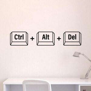 May include: Black and white wall decal of computer keyboard keys that read "Ctrl + Alt + Del" on a white wall. A white desk with a lamp is in the foreground.
