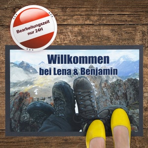 May include: A welcome mat with a mountain scene and the text "Willkommen bei Lena & Benjamin". Two pairs of shoes are on the mat, one pair of yellow sandals and one pair of brown hiking boots.