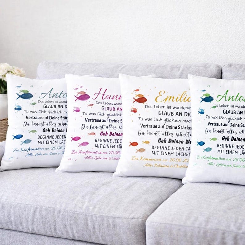 May include: Four white square throw pillows featuring German text and colourful fish illustrations. Each pillow displays a unique name in a script font, followed by inspirational phrases and a date, printed in blue, pink, gold, or green ink.