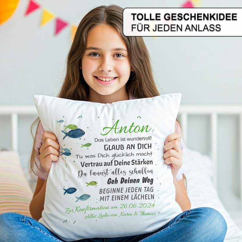 May include: A white square throw pillow featuring a printed design of small blue and green fish. The text reads: Anton, Das Leben ist wundervoll!, GLAUB AN DICH, Tu was Dich gl&uuml;cklich macht, Vertrau auf Deine St&auml;rken, Du kannst alles schaffen, Geh Deinen Weg, BEGINNE JEDEN TAG MIT EINEM L&Auml;CHELN, Zur Konfirmation am 26.06.2024, Alles Liebe von Karin & Thomas.