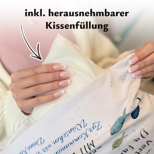 May include: A white pillowcase with a fish pattern and blue text that reads "Zur Kommunion W&uuml;nschen wir" and "Deine", featuring a removable pillow insert. The fabric is white with small blue dots and illustrations of blue and green fish.