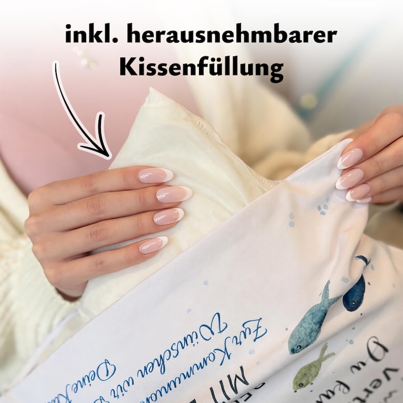 May include: A white pillowcase with a fish pattern and blue text that reads "Zur Kommunion W&uuml;nschen wir" and "Deine", featuring a removable pillow insert. The fabric is white with small blue dots and illustrations of blue and green fish.