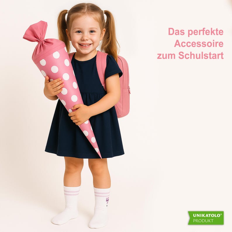 May include: A young girl smiles, holding a pink and white polka-dot school cone. She wears a navy blue dress, pink backpack, and white socks. The text on the right says, "The perfect accessory for the start of school."