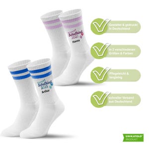 May include: White athletic socks with blue and pink stripes at the top. One pair has blue stripes and the name "Arthur" printed on it, and the other pair has pink stripes and the name "Hanna".