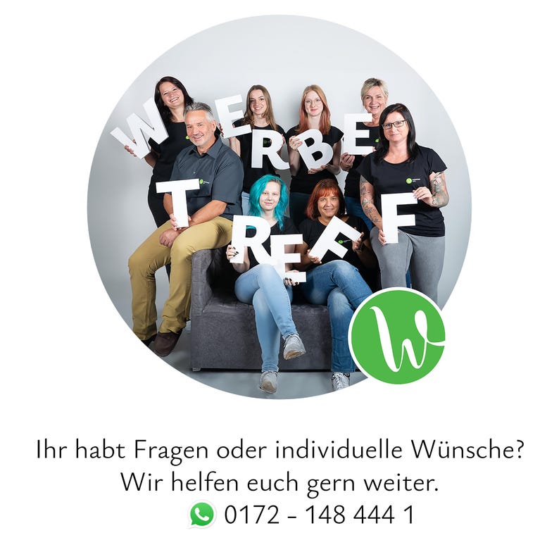 May include: A group of eight individuals posing together, holding large white letters that spell out WERBETREFF. They are dressed in casual clothing, including black t-shirts, jeans, and khaki trousers, positioned around a dark grey sofa.