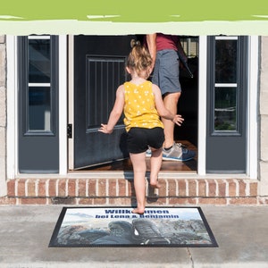 May include: A welcome mat with the text "Willkommen bei Lena & Benjamin" printed on it. The mat is black with a blue and white image of hiking boots on a mountain path.