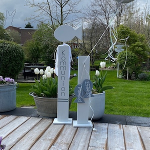 Może przedstawiać: Dwa białe drewniane znaki z kształtem ryby na górze. Znak po lewej stronie mówi "Komunia", a znak po prawej stronie mówi "Matthias". Srebrny balon z tekstem "Alles Liebe zur Kommunion" unosi się w tle.