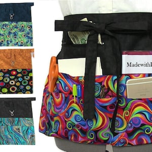 以下が含まれることがあります： 複数のポケットが付いた黒いユーティリティエプロン用の3つの異なるファブリックパターン。エプロンは、タイクロージャー付きの黒いウエストバンドが付いています。エプロンは、白いシャツを着た人が着用している様子が示されています。エプロンに書かれたテキストは「Made with Love 4 Hopes」です。