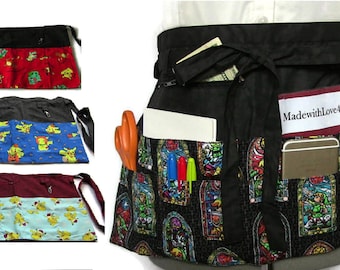 May include: Three different patterned waist aprons with multiple pockets. The aprons are black, gray, and burgundy with a variety of colorful patterns. The aprons have a zippered pocket on the back and multiple pockets on the front. The aprons are tied at the waist with long ties.