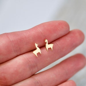 Könnte beinhalten: Ein Paar goldfarbene Lama-Ohrstecker. Die Ohrringe sind klein und zart und haben ein schlichtes, minimalistisches Design.