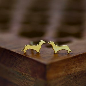 Könnte beinhalten: Ein Paar goldene Ohrringe mit Dachshund-Silhouette. Die Ohrringe sind klein und zart und perfekt, um jedem Outfit einen Hauch von Verspieltheit zu verleihen.