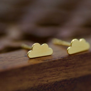 Puede incluir: Un par de pendientes de botón en forma de nube de oro. Los pendientes son pequeños y delicados, y serían un gran regalo para alguien que ama la joyería minimalista.