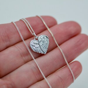 May include: A silver chain necklace with a heart-shaped pendant featuring detailed angel wings.