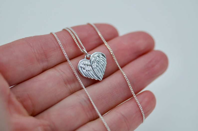 May include: A silver chain necklace with a heart-shaped pendant featuring detailed angel wings.