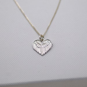 May include: A silver necklace with a heart-shaped pendant featuring detailed angel wings.