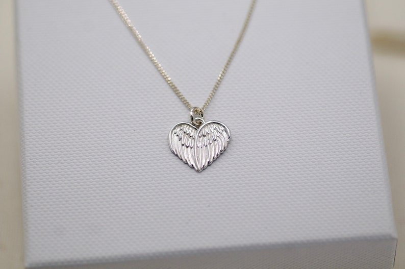 May include: A silver necklace with a heart-shaped pendant featuring detailed angel wings.