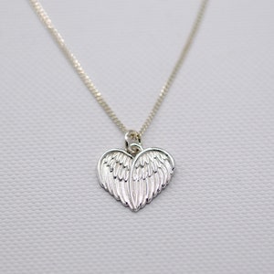 May include: A silver necklace with a heart-shaped pendant featuring detailed angel wings.