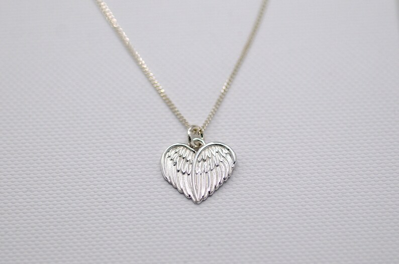 May include: A silver necklace with a heart-shaped pendant featuring detailed angel wings.