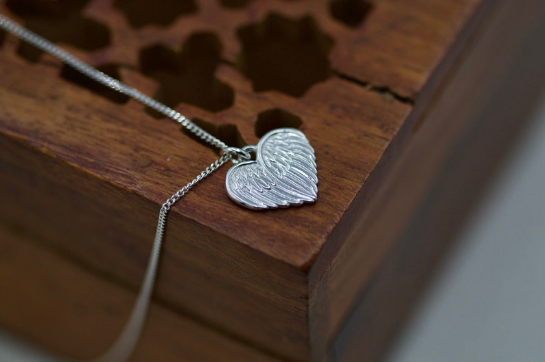 May include: A silver necklace with a heart-shaped pendant featuring detailed angel wings.