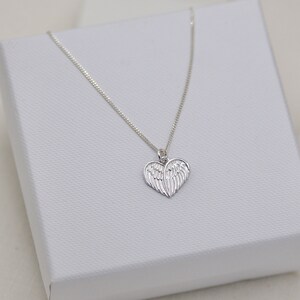 May include: A silver necklace with a heart-shaped pendant featuring angel wings.