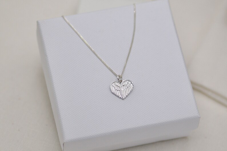 May include: A silver necklace with a heart-shaped pendant featuring angel wings.