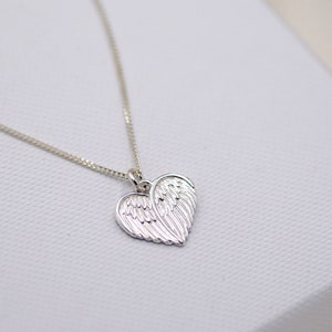 May include: A silver necklace with a heart-shaped pendant featuring a detailed design of angel wings.