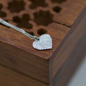 May include: A silver necklace with a heart-shaped pendant featuring detailed angel wings.