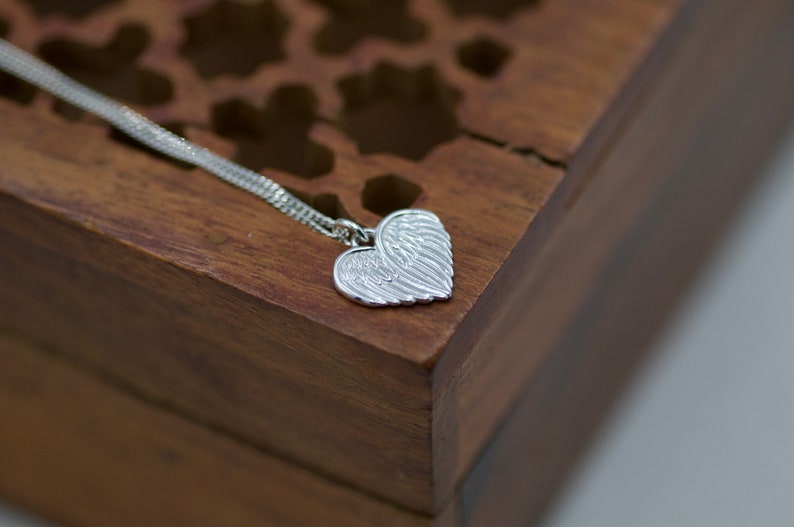 May include: A silver necklace with a heart-shaped pendant featuring detailed angel wings.