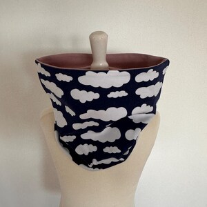 Könnte beinhalten: Ein marineblauer Rundschal mit weißem Wolkenmuster. Die Innenseite ist in einem zarten Rosa gehalten. Der Rundschal wird auf einer Schaufensterpuppe präsentiert. Ein gemütliches Accessoire für kaltes Wetter.