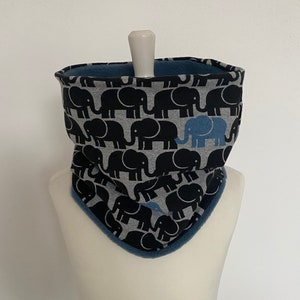 Könnte beinhalten: Ein Nackenwärmer mit grauem und schwarzem Elefantenmuster und blauem Fleecefutter. Der Nackenwärmer wird auf einer Schaufensterpuppe präsentiert. Der Elefantenaufdruck enthält einen blauen Elefanten.