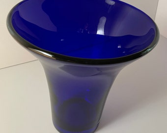May include: A cobalt blue glass vase with a flared opening and a rounded base. The vase is made of thick glass and has a glossy finish.