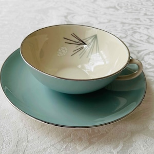 Könnte beinhalten: Ein hellblaues Teetassen- und Untertassen-Set mit silbernem Rand. Die Teetasse hat ein weißes Inneres mit einem schwarz-weißen geometrischen Design einer Kiefernzapfen.